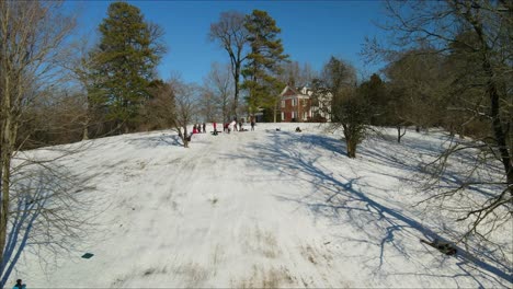 aerial footage of kids snow sledding the side of a steep hill