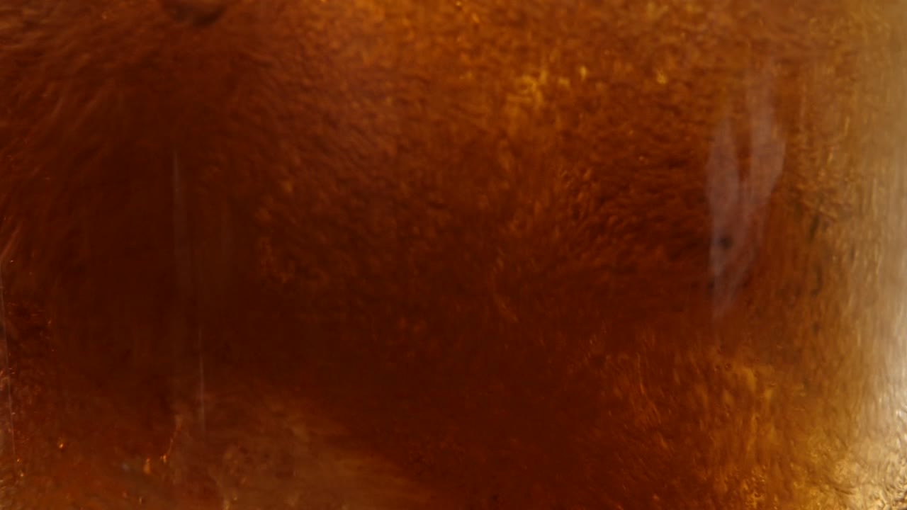 toma macro de cubitos de hielo redondos en un vaso mientras se vierte una refrescante cola sobre ellos