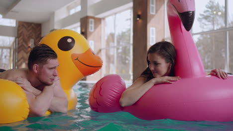 happy man and woman are resting together in swimming pool in hotel floating on inflatable swimming circles