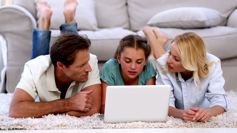 padres e hija felizmente usando la computadora portátil en el suelo