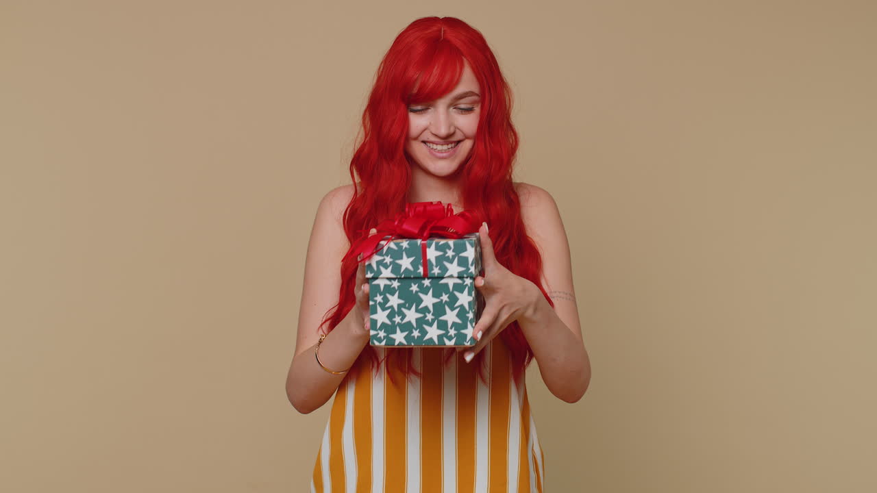 Ragazza dai capelli rossi vincitrice riceve un bonus in una confezione regalo, una sorpresa di compleanno, esprimendo grande felicità e stupore.
