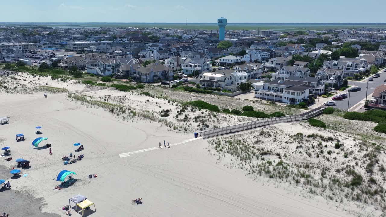 Aerial view of Stone Harbor, NJ. Elegant beachfront homes and coast behind wide sandy beach with dunes, umbrellas and walkways. Classic East Coast summer scene under clear skies. Wide shot