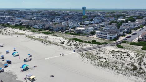 aerial view of stone harbor, nj. elegant beachfront homes and coast behind wide sandy beach with dunes, umbrellas and walkways. classic east coast summer scene under clear skies. wide shot