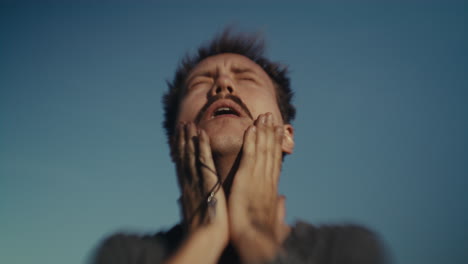 man expressing strong emotion against a clear blue sky