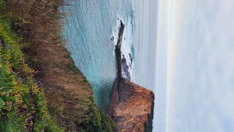 Zambujeira-do-Mar-over-the-sea-shore-with-ocean-waves,-cliffs-and-sand-dunes-covered-by-green-vegetation-red-leaves-of-sour-fig,-sunny-day,-clear-blue-sky