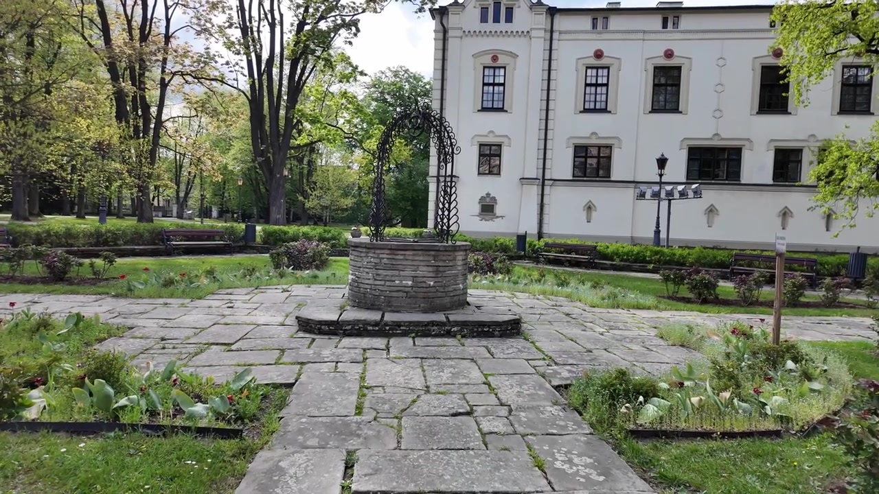 Een grijze stenen put in een levendige tuin, omringd door planten en bomen, met historische kasteelgebouwen zichtbaar op de achtergrond.