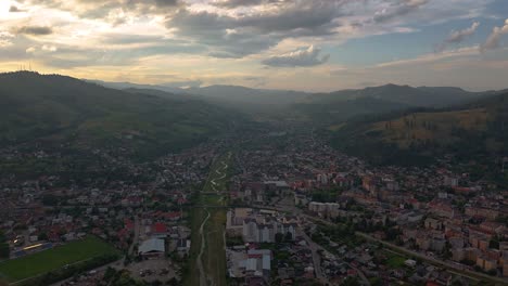 drone hyperlapse shows gura humorului's rooftops and mountains under a colorful sunset sky