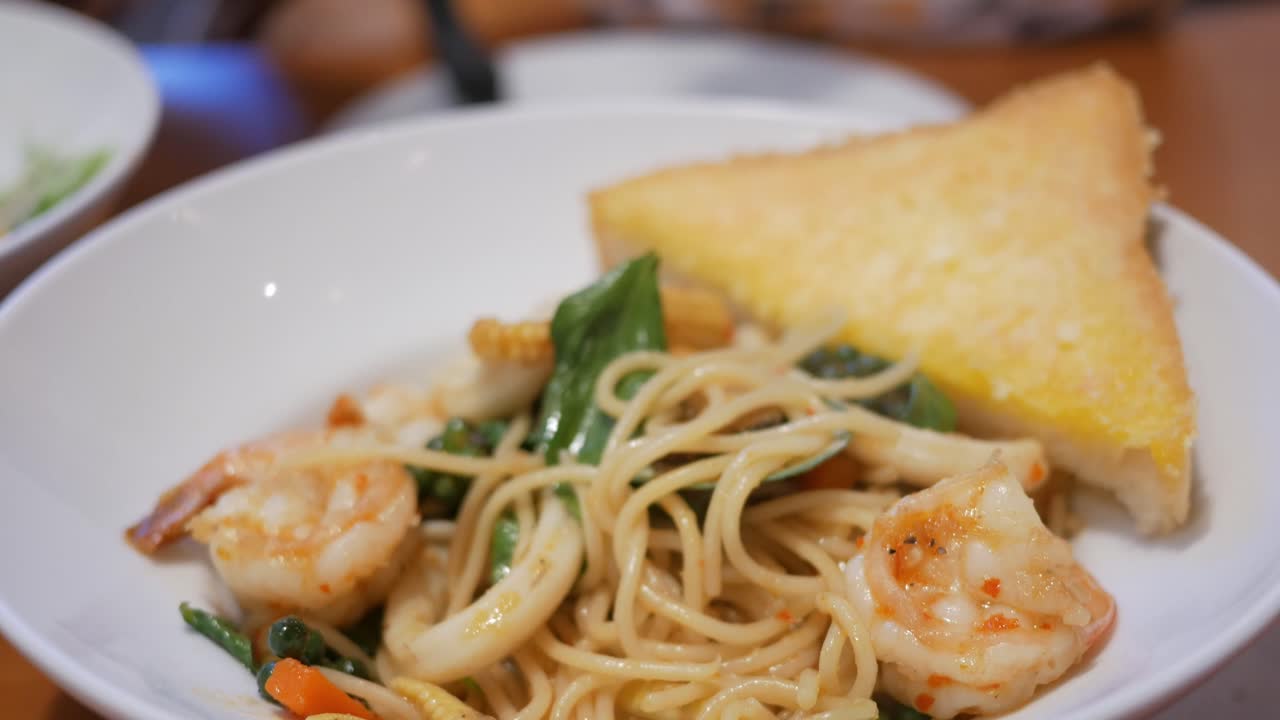 해산물 파스타 와 버터 로 된 토스트 로 가득 찬 접시 에 휘어지는 포크 로 스파게티 를 휘두르는 것