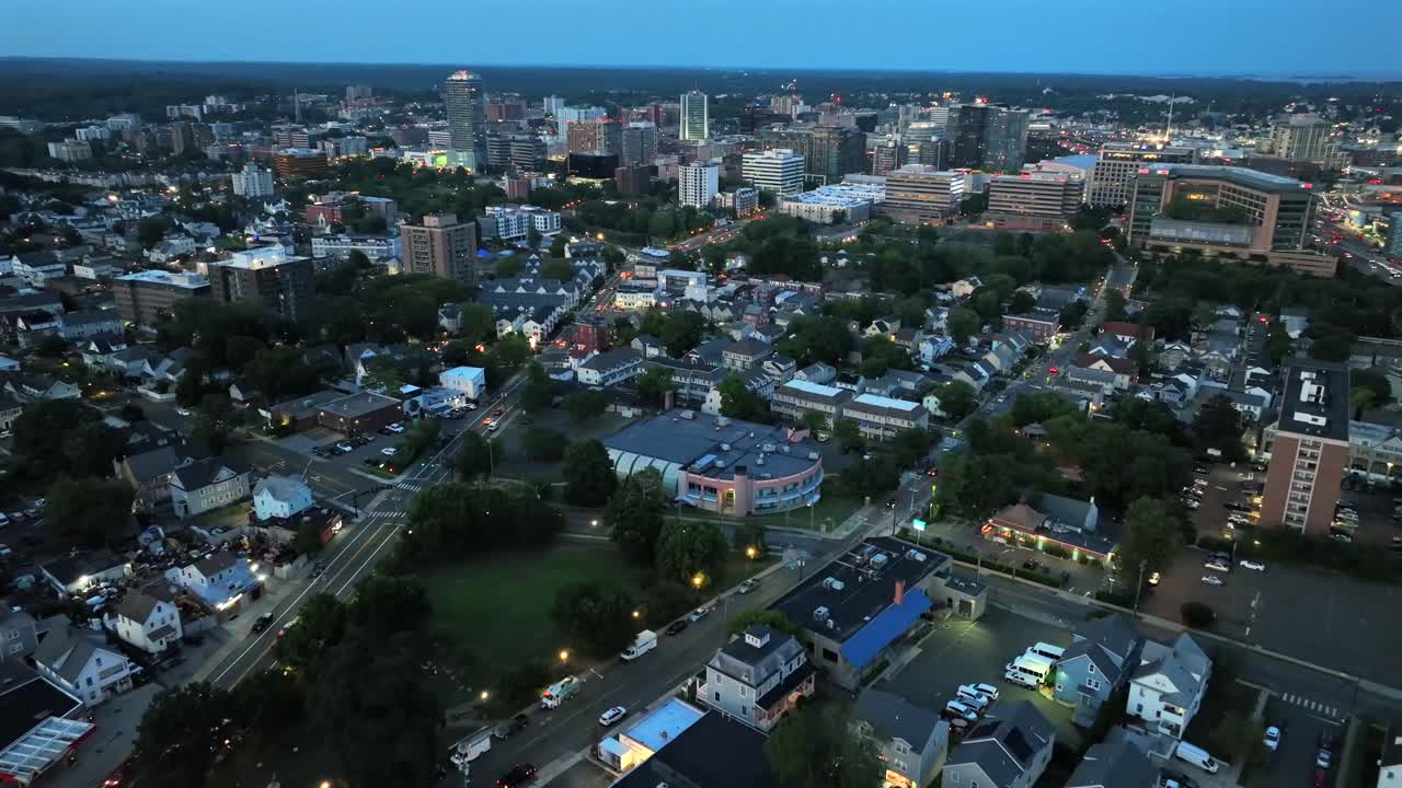 Quartiere periferico e paesaggio urbano di una città americana al tramonto. Scena notturna in estate. Il centro di Stamford, Connecticut, sullo sfondo. Volo aereo all'indietro. Ripresa aerea dei tetti delle case.