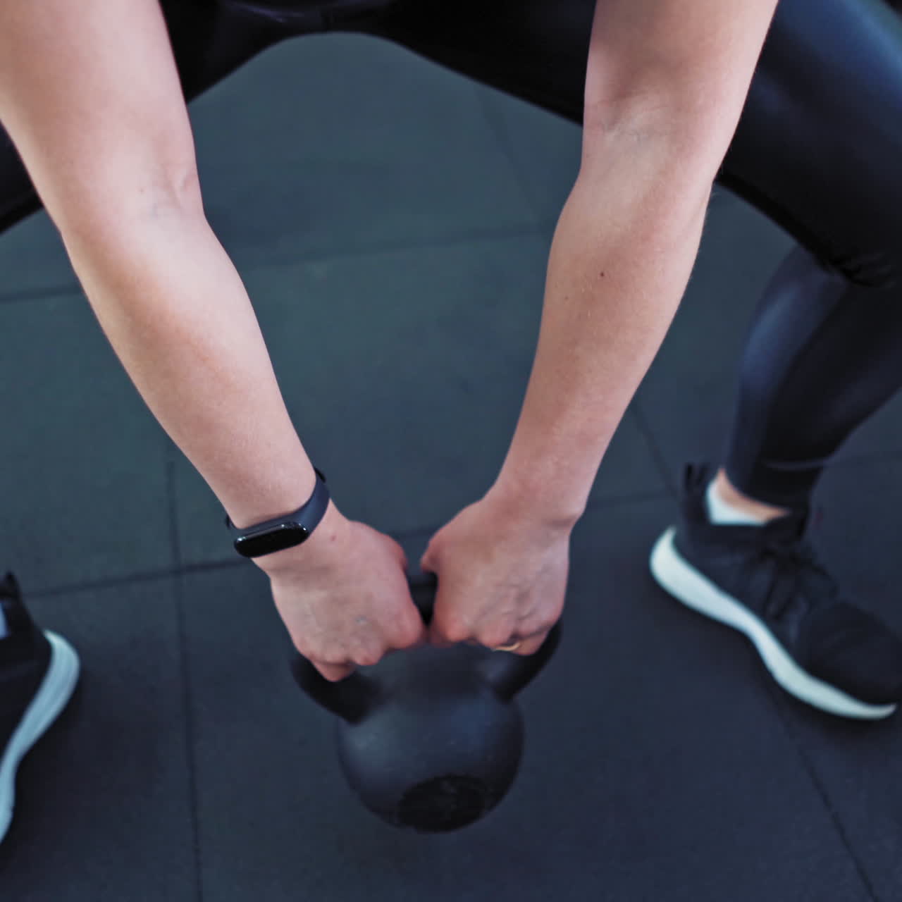 Close-up of a strong musular female's body with kettlebell. Athlete woman wearing black top and leggings lifting hard weight in sports club.