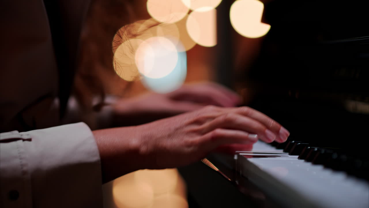 Close up of a woman's hands playing the piano with blurry lights on the background