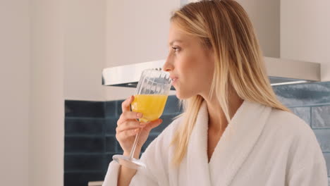 una mujer rubia bebiendo jugo de naranja en la cocina.