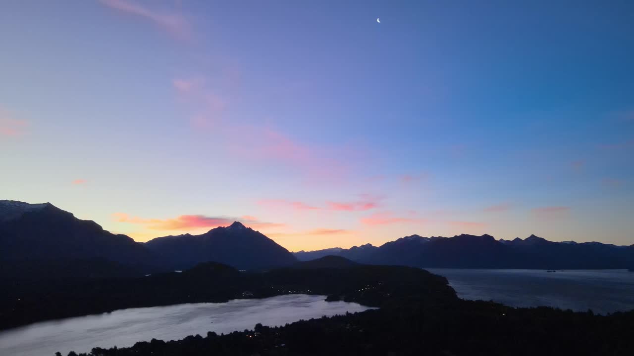 Pan shot of the meeting between the sunset and the crescent moon over the Nahuel Huapi lake as the stage. Patagonia, Argentina. Aerial Footage