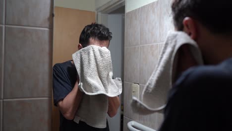 man drying his wet face with towel after washing in the bathroom