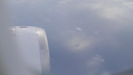 Passenger plane wing view over clouds, showing calm sky from window seat POV