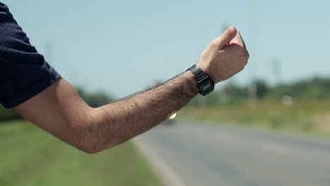 man points thumb to hitchhike on roadside, close-up