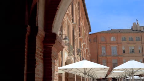 Der-Stadtplatz-Von-Montauban-Mit-Sonnenschirmen-Und-Architektonischen-Backsteinbögen,-Blick-Auf-Den-Dolly-Rechts