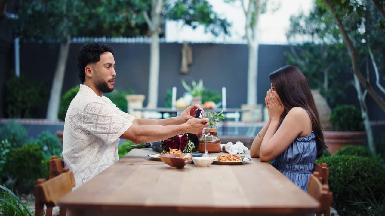 Uomo che fa la proposta di matrimonio a una donna con un anello di fidanzamento durante una cena all'aperto