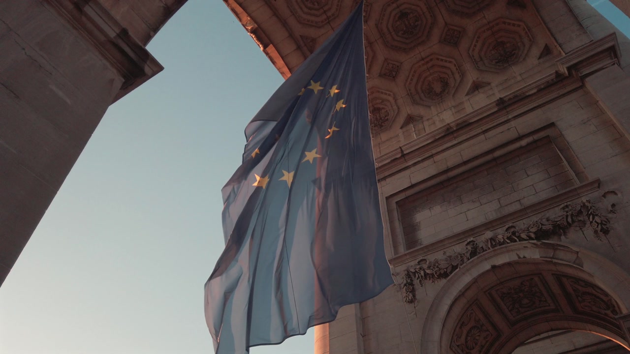 Slow motion view of European Union flag waving beneath Cinquantenaire Arch in Brussels at sunset