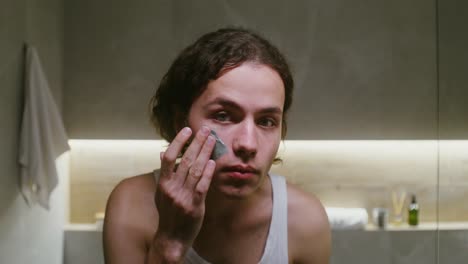 man applying clay face mask in bathroom