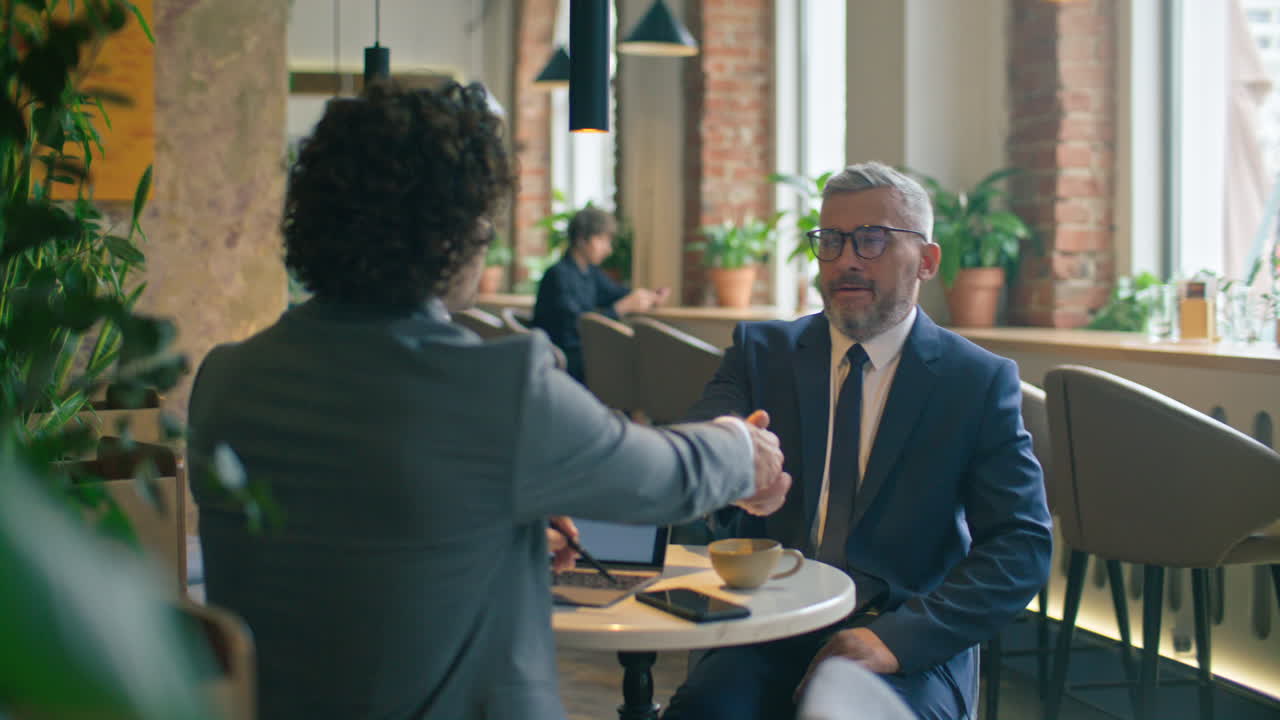 Businessmen Shaking Hands and Discussing Project during Meeting in Cafe