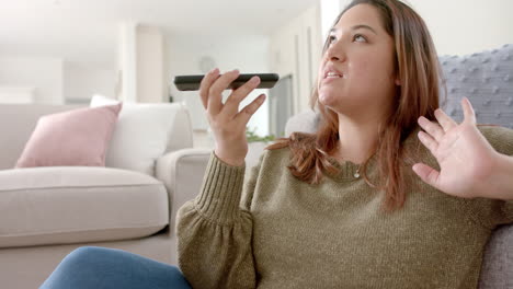 mujer biracial feliz de tamaño plus relajándose en la sala de estar hablando en teléfono inteligente, cámara lenta