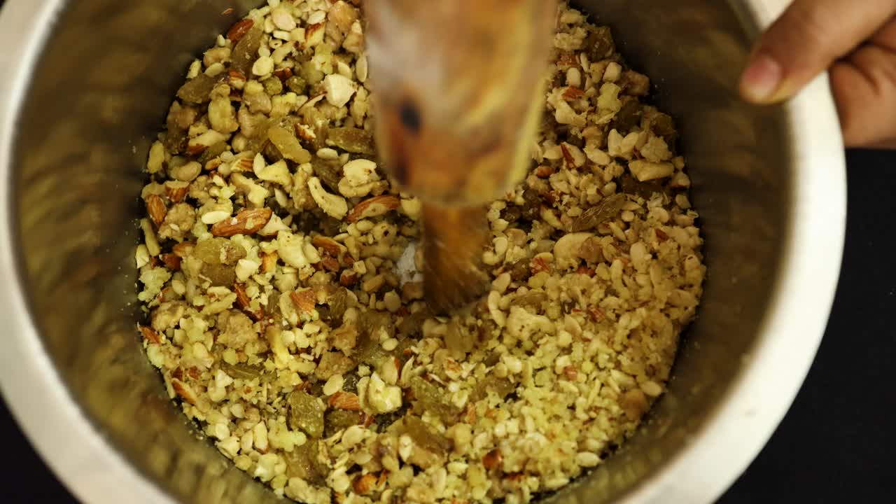 Top view of person grinding assorted nuts in metal bowl for dessert