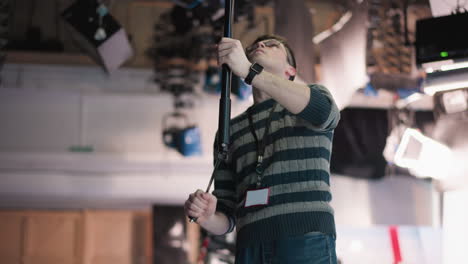 overhead view of stage lighting in broadcast studio. lighting equipment hanging from ceiling, adjusted by technician using boom pole to set up production for filming