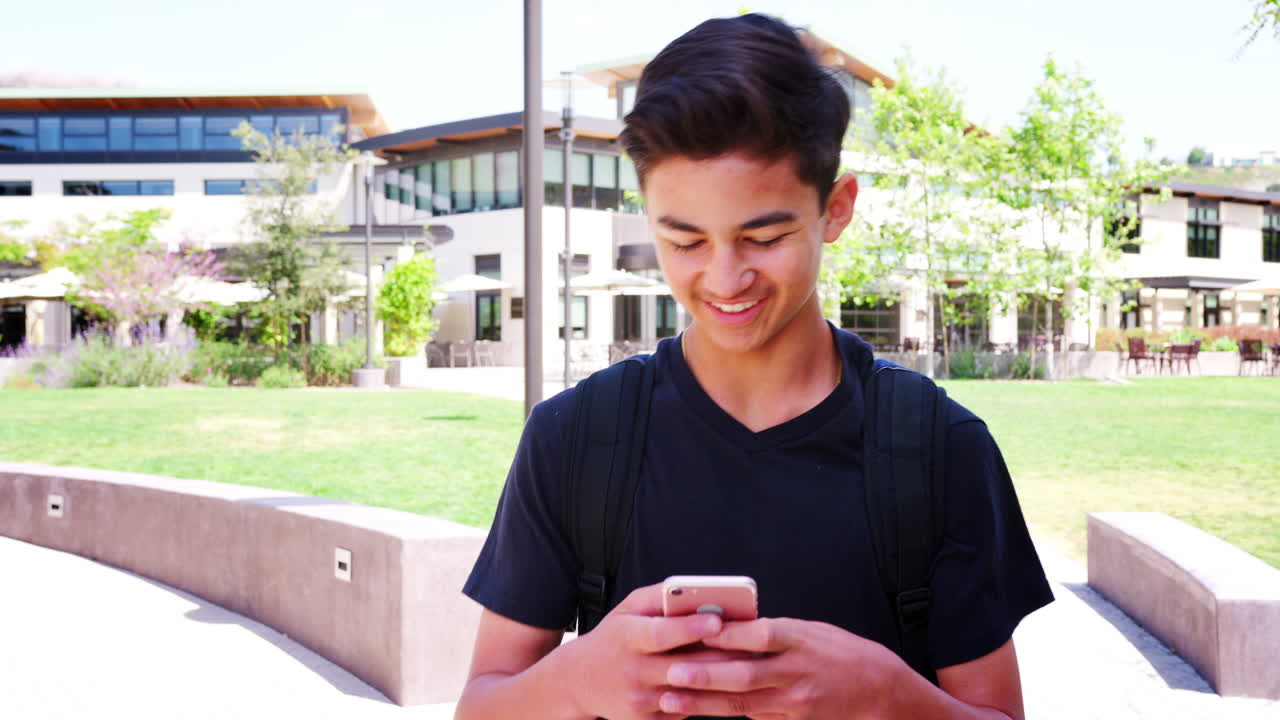 남성 고등학교 학생이 대학 건물 밖에서 휴대폰으로 메시지를 확인하고 있습니다.