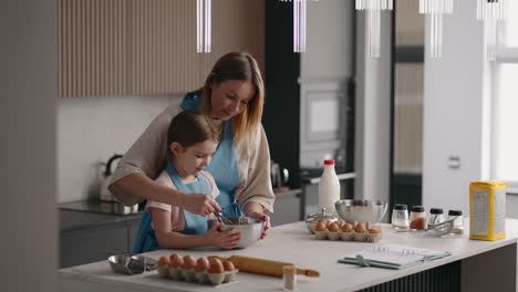 cooking at home mother and little daughter are cooking dough for pancakes or cake mixing ingredients