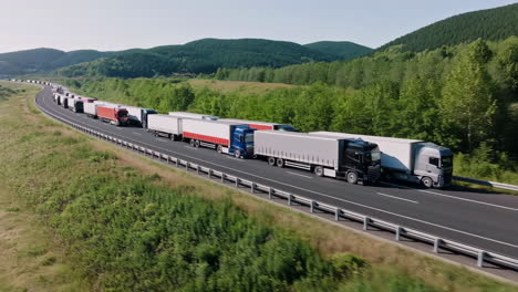 long convoy of semi-trucks on a winding highway through a green landscape