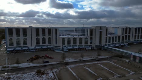 large distribution center with loading docks and parking lot under a cloudy sky in winter. breathtaking aerial view flight ascending drone