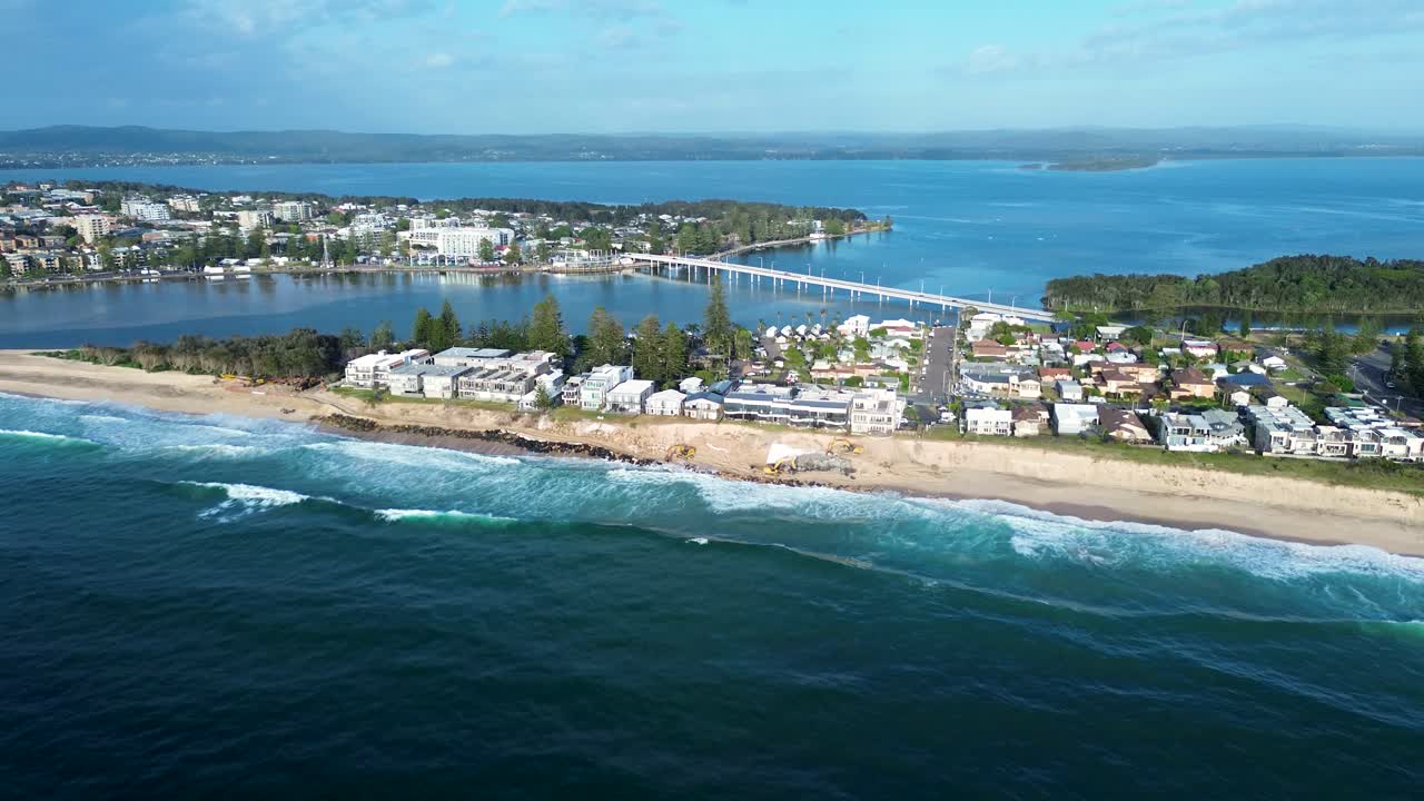 Drone aerial landscape of ocean waves breaking on rocky break wall with The Entrance beach town bridge and suburban housing beside Tuggerah Lake Central Coast Australia travel tourism nature outdoors