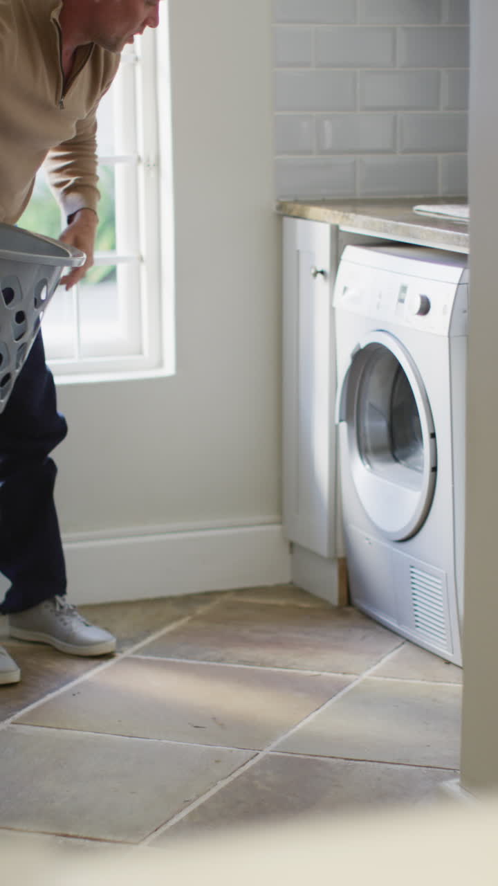 video vertical de un hombre caucásico feliz sosteniendo una canasta y lavando la ropa en la cocina