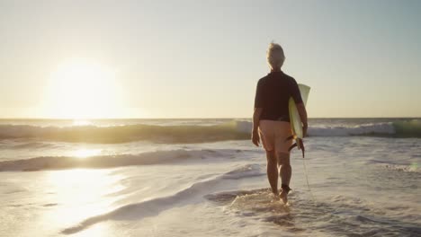 Hombre-Mayor-Caminando-Con-Tabla-De-Surf-En-La-Playa