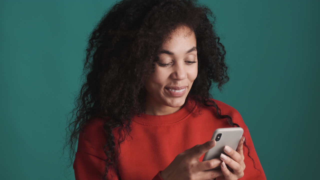 African american smiling woman using smartphone over blue background.