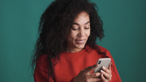 una mujer afroamericana sonriente usando un teléfono inteligente sobre un fondo azul.
