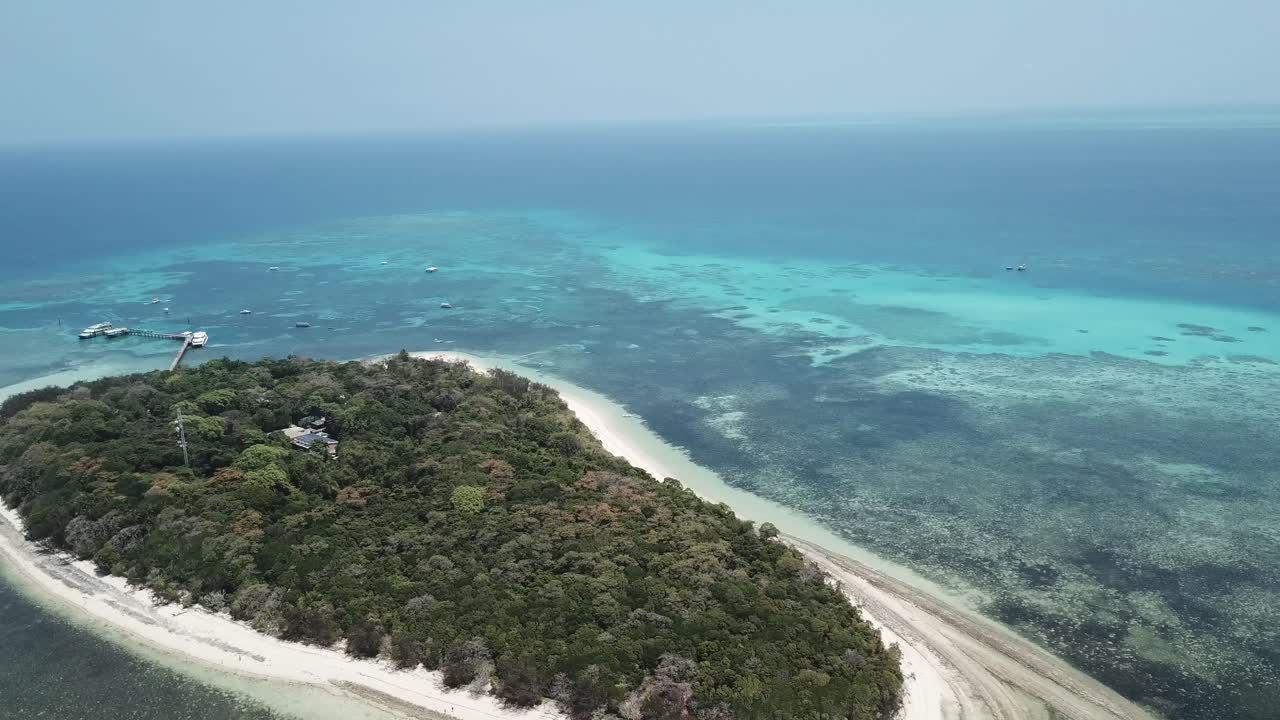 Riprese aeree con drone su una piccola isola tropicale con foresta attorno a una barriera corallina limpida e blu.