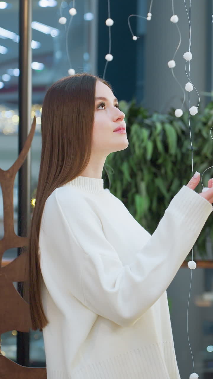 Lady standing and gently touching Christmas tree decorations, with illuminated festive ornaments and a Santa Claus figure in the background