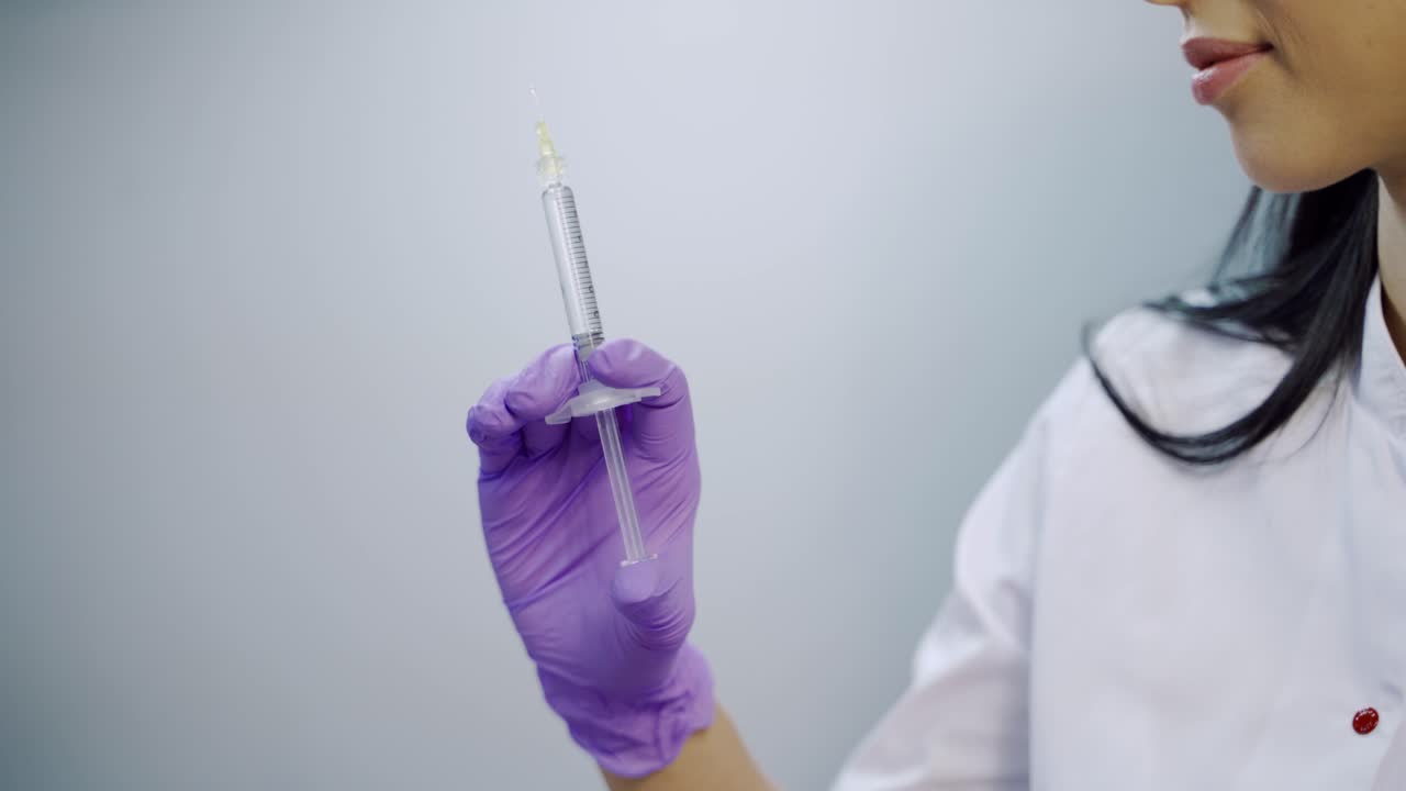A beautician in purple gloves is holding an injection of a botulinum toxin in her hand at a medical cosmetology center. Close-up. Preparation to the procedure
