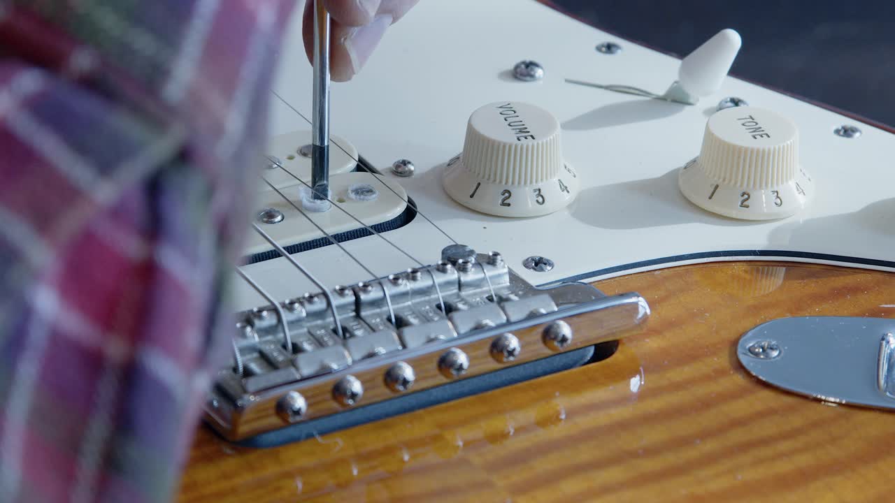 Cera dal pickup di una chitarra elettrica mentre un tecnico di chitarre regola la vite del pickup
