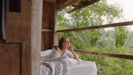 attractive woman lying in bed at hotel resort feeling playful smiling enjoying vacation relaxing in comfort with view of tropical jungle