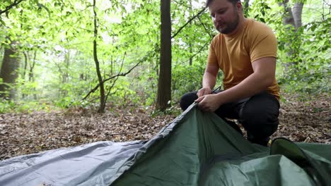 Young-camper-adding-metal-frame-to-tent-fabric-in-forest,-front-view