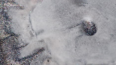 macro view of glittery grey inks blending as a milky liquid swirls in, creating fluid abstract patterns