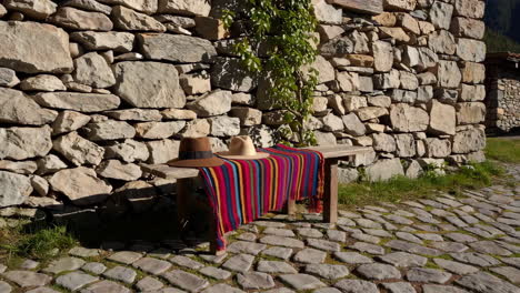wooden bench with hats and textile in front of a stone wall