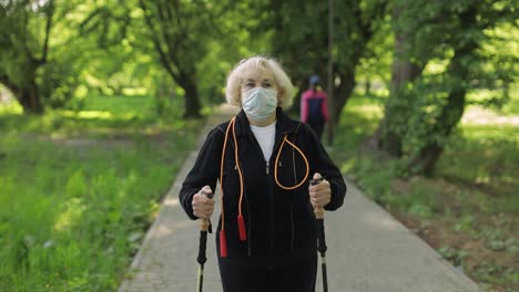 senior woman walking in the park with a face mask and walking sticks