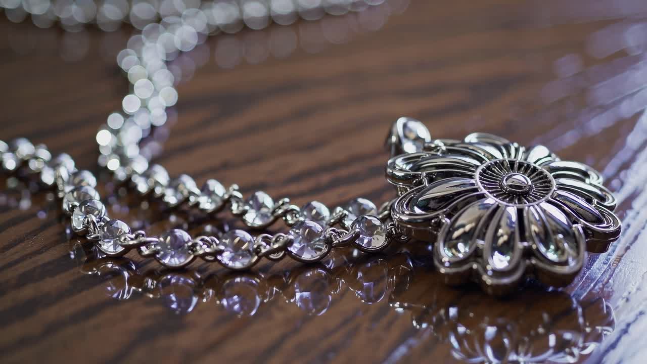 Close-up video shot of a silver floral pendant necklace on a wooden surface, showcasing intricate