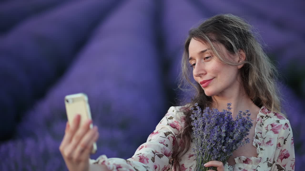Una giovane donna gioiosa si scatta un selfie mentre tiene in mano un bouquet di lavanda in un campo viola
