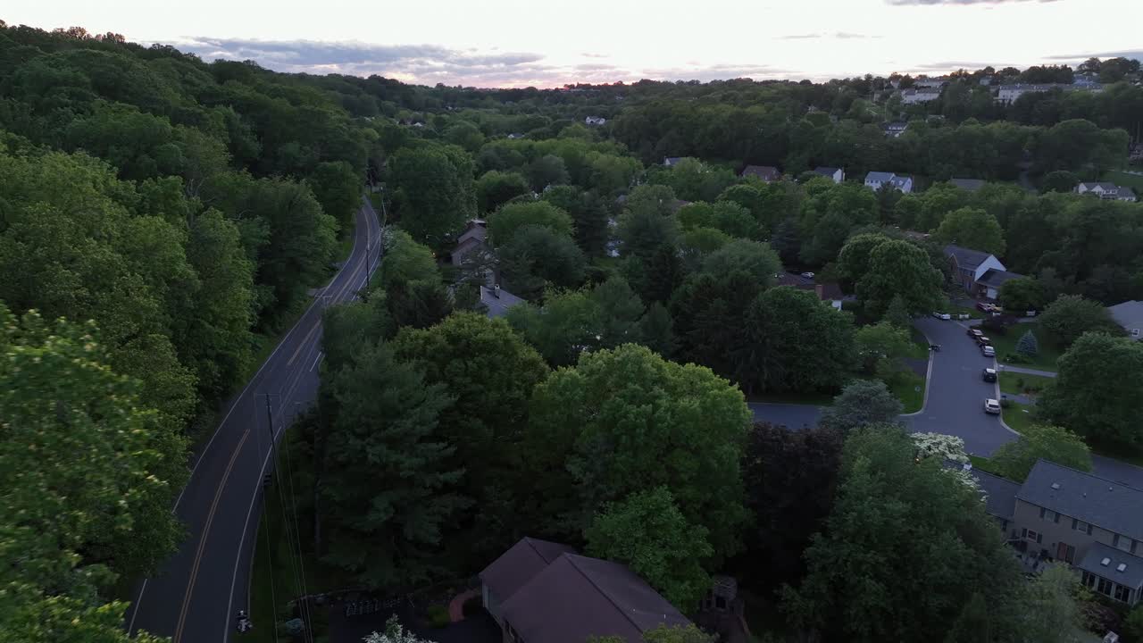 Drone flight over green trees on American suburb neighborhood located on hill. Cloudy day in summer. Aerial landing shot. Community of kind suburb district.