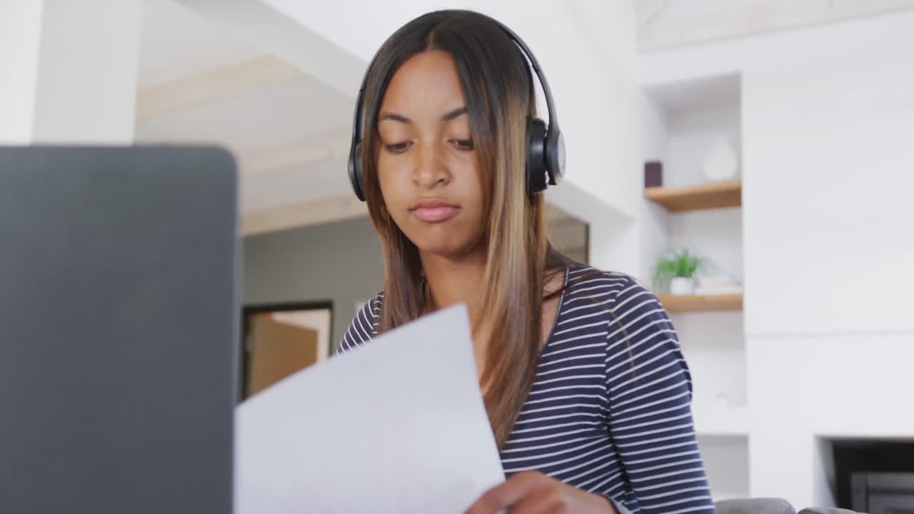 una adolescente biracial con auriculares y usando una computadora portátil en casa, en cámara lenta